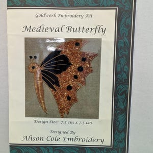 May include: A goldwork embroidery kit titled "Medieval Butterfly." The design features a butterfly with black and gold wings. The design size is 7.5 cm x 7.5 cm. Designed by Alison Cole Embroidery. The kit is framed with a dark green border.