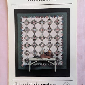 May include: A printed pattern titled "Wildflower" by thimbleberries. The cover features a quilt design with floral patterns in a diamond grid, a small bench, and a basket of flowers. The background is a dark green.