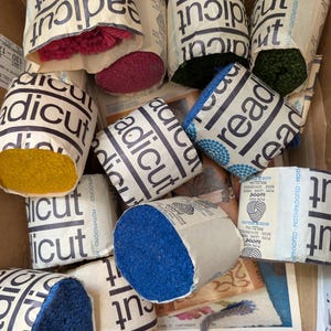 May include: A collection of wrapped yarn balls in various colors, including pink, green, blue, and yellow. The packaging features the text "radicut" and "read". The yarn is displayed in a cardboard box.