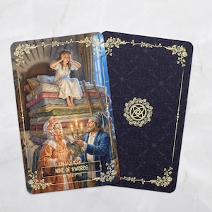 Pu&ograve; includere: Due carte dei tarocchi. La carta anteriore raffigura una scena con una persona su una pila di materassi e due persone che tengono candele. La carta &egrave; etichettata "NINE OF SWORDS". La carta posteriore &egrave; blu scuro con un bordo floreale dorato e un simbolo.