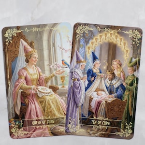 Pu&ograve; includere: Due carte dei tarocchi con illustrazioni di reali. La carta "Queen of Cups" raffigura una donna in abito rosa e oro, mentre la carta "Ten of Cups" mostra una famiglia reale con un bambino. Entrambe le carte hanno bordi floreali e testo.