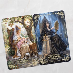 Pu&ograve; includere: Due carte dei tarocchi illustrate. Una carta mostra una donna in abito dorato che tiene in braccio un bambino, con la scritta "III. L'Imperatrice". L'altra carta raffigura una donna in abito nero che tiene uno specchio, con la scritta "Queen of Swords".