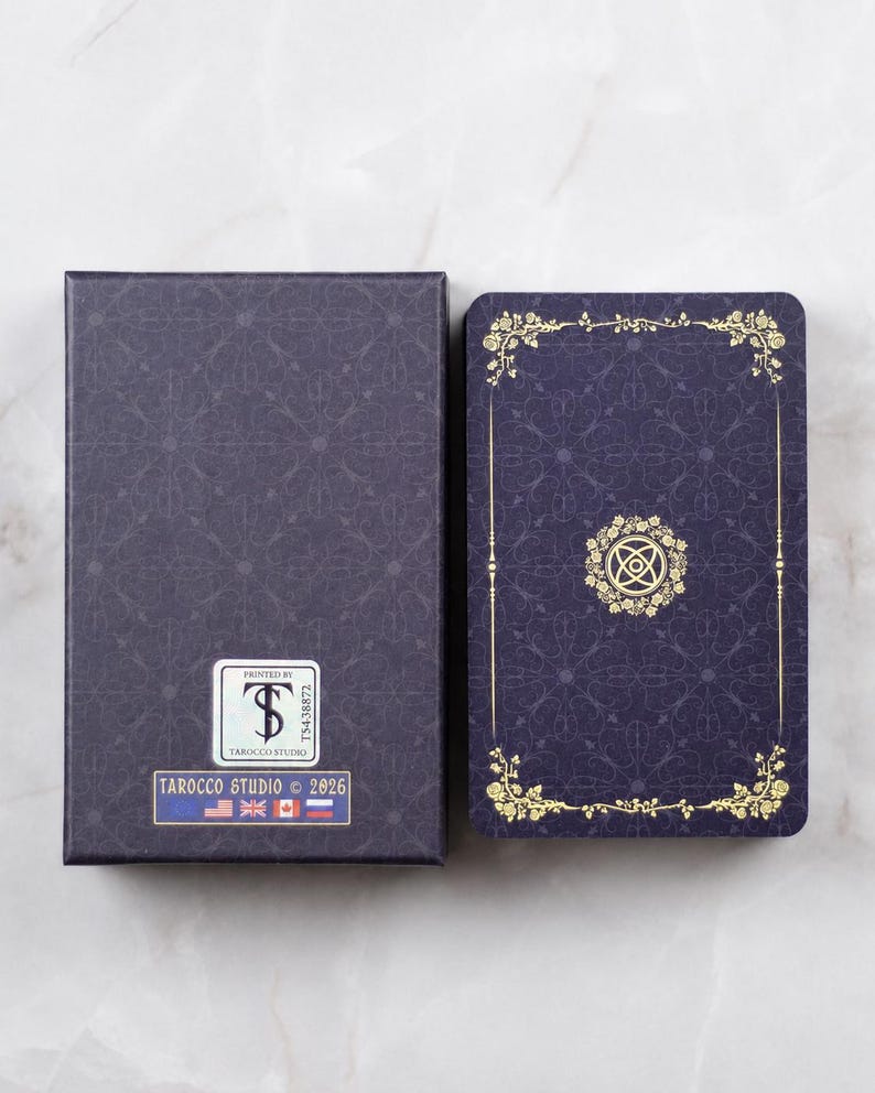 Pu&ograve; includere: Un mazzo di tarocchi e un set di scatole. La scatola e i dorsi delle carte sono blu scuro con un motivo ripetuto. I dorsi delle carte hanno accenti floreali dorati e un emblema centrale. La scatola ha un adesivo che recita "TAROCCO STUDIO &copy; 2026".