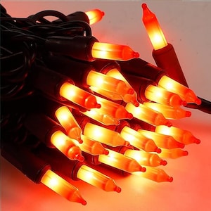 May include: A string of orange Christmas lights with black wire. The lights are lit and glowing.