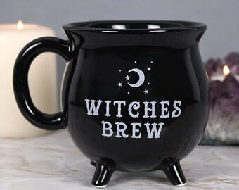 May include: Black ceramic cauldron mug with a white crescent moon and stars design. The mug has a handle and three legs. The text "Witches Brew" is printed on the front.