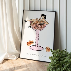 Puede incluir: Una ilustración enmarcada de una mujer sentada en una copa de tallo rosa llena de macarons naranja y rosa. El texto debajo de la imagen dice "dame au macaron et fromage".
