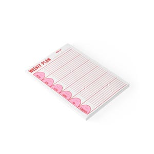 May include: A white weekly plan notepad with pink text and lines. The words "WEEKLY PLAN" are printed in pink at the top left. Days of the week are listed in pink, with lines for notes. The notepad is angled on a white background.
