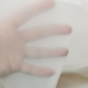May include: A close-up of a sheer white fabric, showing its texture and translucency. The fabric is soft and delicate, with a slightly crinkled appearance.