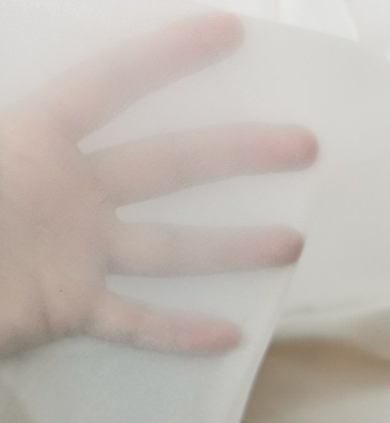 May include: A close-up of a sheer white fabric, showing its texture and translucency. The fabric is soft and delicate, with a slightly crinkled appearance.