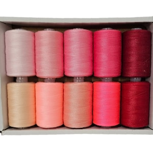 May include: A set of ten spools of thread in various shades of pink and red. The spools are arranged in a gradient from light pink to dark red.