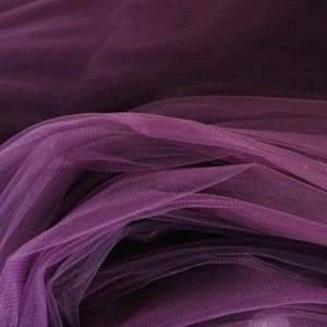 May include: Purple tulle fabric with a soft, delicate texture. The fabric is draped and folded, creating a flowing and elegant look.