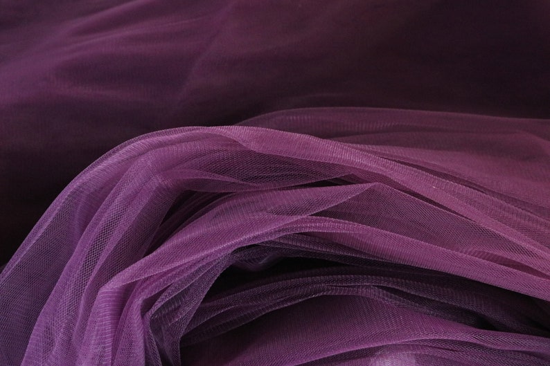 May include: Purple tulle fabric with a soft, delicate texture. The fabric is draped and folded, creating a flowing and elegant look.
