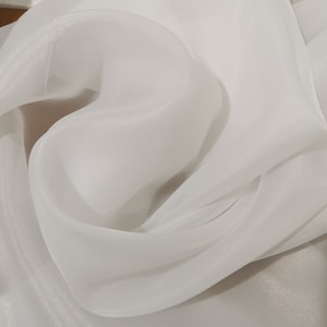 May include: White sheer fabric with a soft, flowing texture. The fabric is draped and folded, creating a delicate and elegant look.