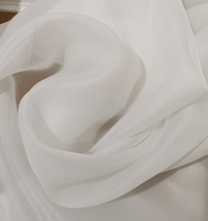 May include: White sheer fabric with a soft, flowing texture. The fabric is draped and folded, creating a delicate and elegant look.