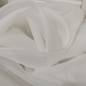 May include: White sheer fabric with a soft, flowing texture. The fabric is draped and folded, creating a delicate and airy appearance.