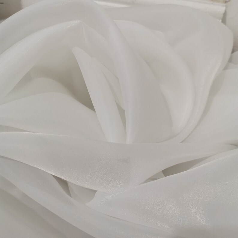 May include: White sheer fabric with a soft, flowing texture. The fabric is draped and folded, creating a delicate and airy appearance.