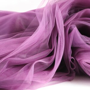 May include: A close-up of a soft, purple tulle fabric. The fabric is draped and folded, creating a delicate and airy texture.