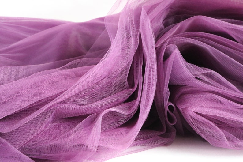 May include: A close-up of a soft, purple tulle fabric. The fabric is draped and folded, creating a delicate and airy texture.