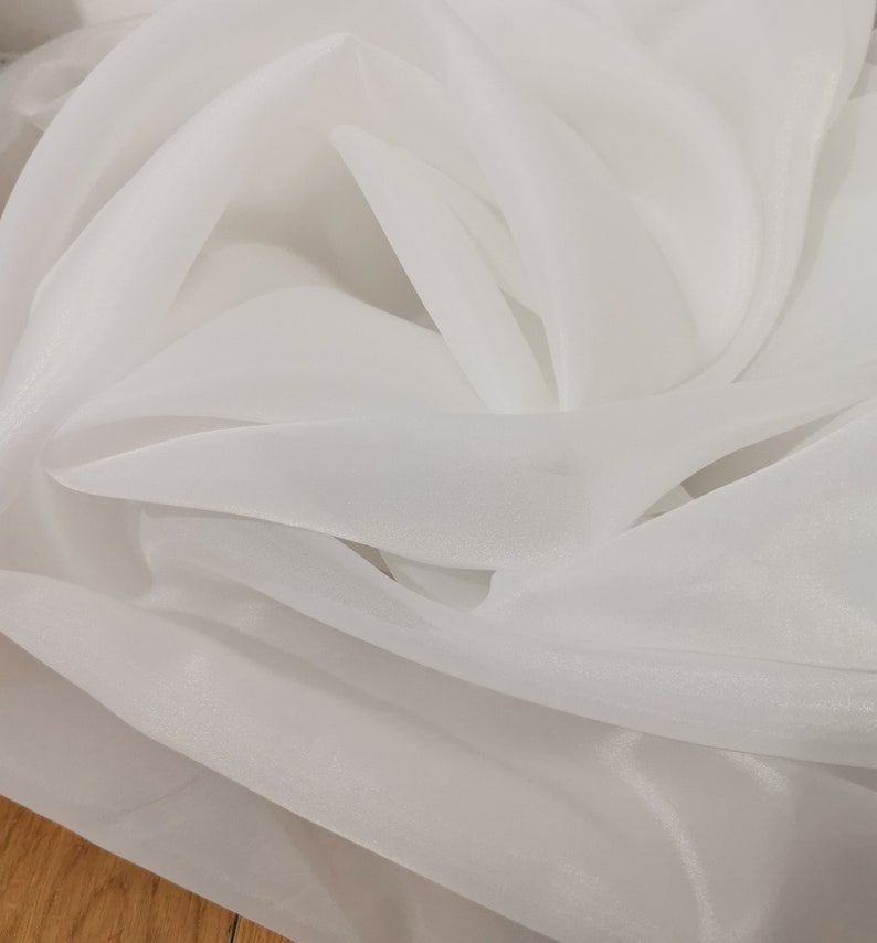 May include: White sheer fabric with a soft, flowing texture. The fabric is translucent and has a subtle sheen.