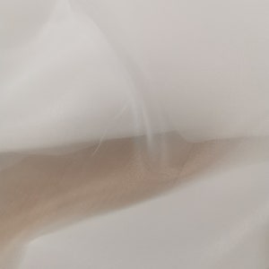 May include: White sheer fabric with a soft, flowing texture. The fabric is draped and folded, creating a delicate and airy appearance.