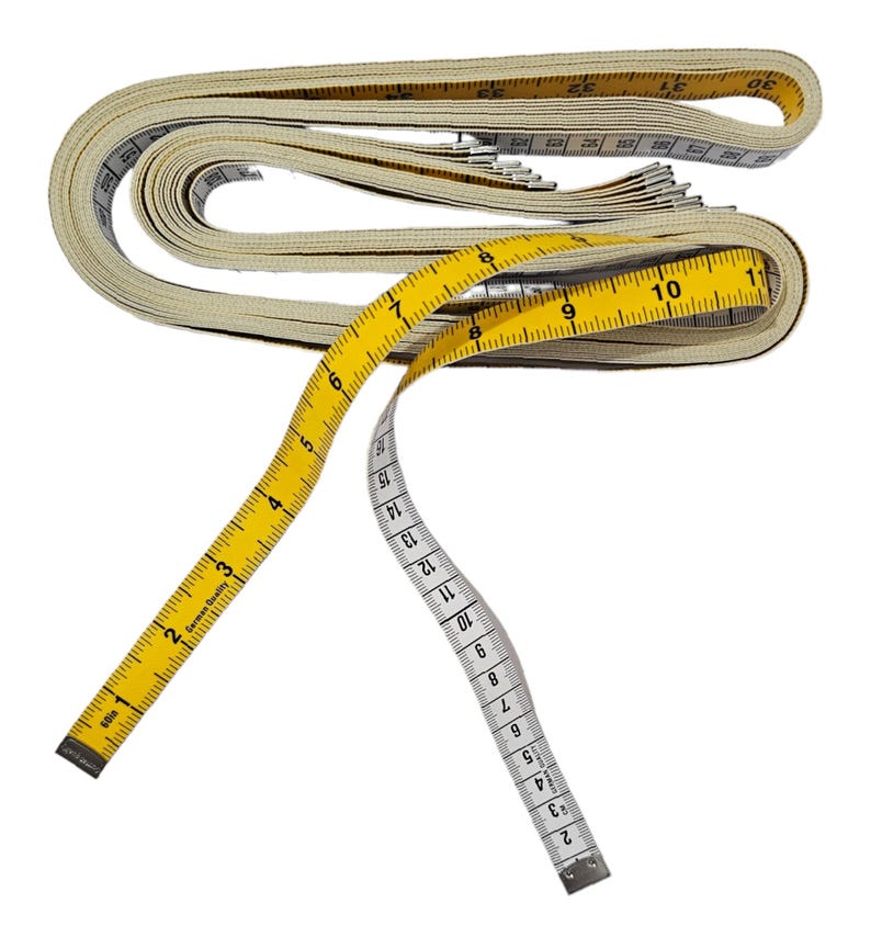 May include: A yellow and white measuring tape with a white fabric casing. The tape is coiled and the end of the tape is extended. The tape has numbers from 1 to 30 printed on it.