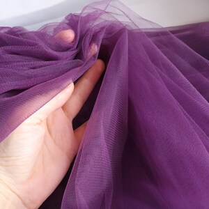 May include: Purple tulle fabric with a soft, delicate texture. The fabric is sheer and has a fine mesh weave.