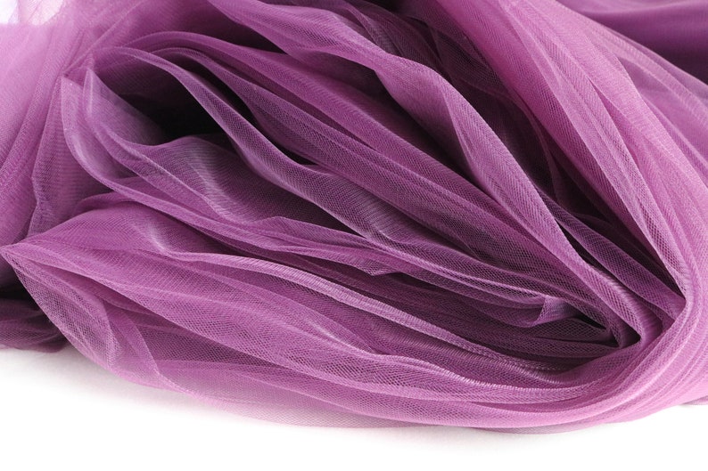 May include: A close-up of a soft, purple tulle fabric. The fabric is draped and folded, creating a delicate and airy texture.