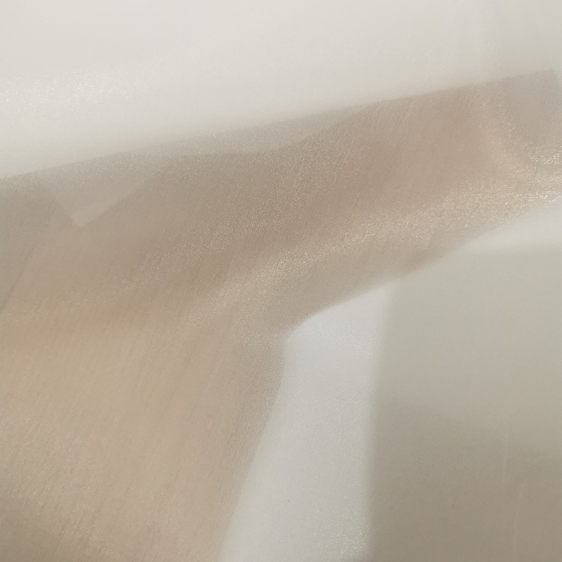 May include: A piece of sheer, light brown fabric with a subtle shimmer. The fabric is draped over a white surface.