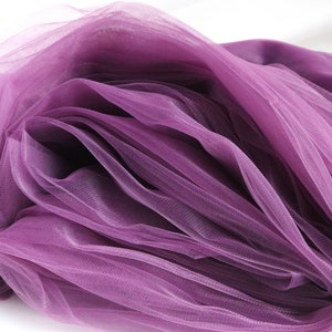 May include: Purple tulle fabric with a soft, delicate texture. The fabric is folded and draped, showcasing its sheer and airy quality.