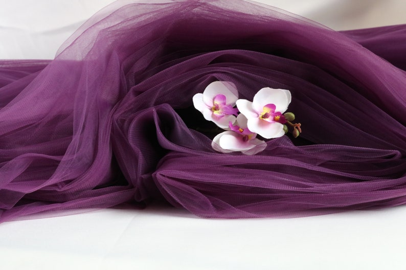 May include: Purple tulle fabric with white orchids with pink centers.