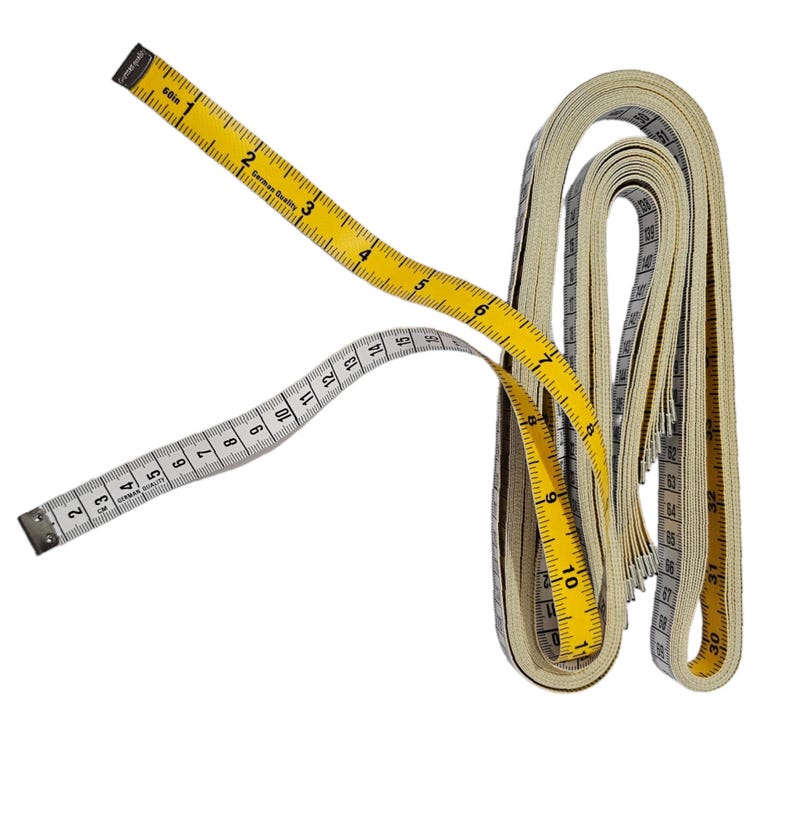 May include: Two measuring tapes, one yellow and one white, are rolled up together. The yellow tape has black markings and the text "German Quality" printed on it. The white tape has black markings and the text "30m" printed on it.