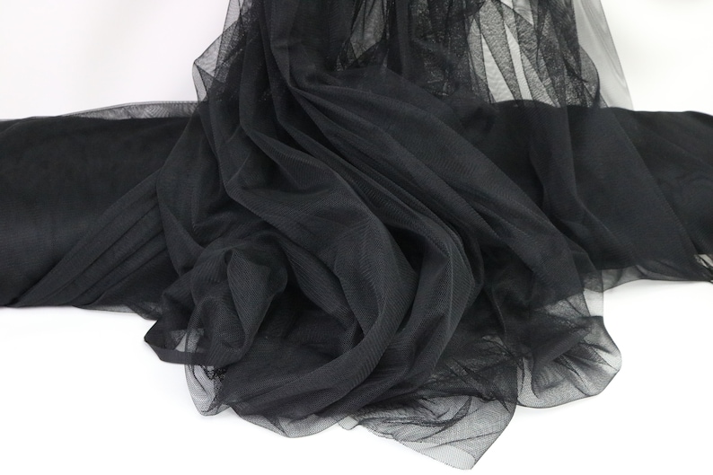 Puede incluir: Un rollo de tela de tul negro, exhibido sobre un fondo blanco. La tela est&aacute; suelta, mostrando su fina textura de malla y su color negro intenso. Ideal para proyectos de manualidades y decoraci&oacute;n.