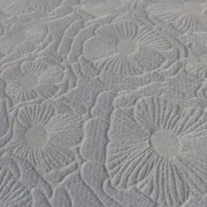 Puede incluir: Primer plano de una tela gris texturizada con un patr&oacute;n repetitivo de formas de flores en relieve.