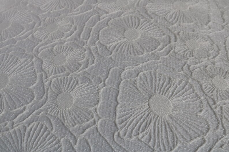Puede incluir: Primer plano de una tela gris texturizada con un patr&oacute;n repetitivo de formas de flores en relieve.