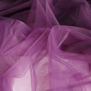 May include: Purple tulle fabric with a soft, delicate texture. The fabric is draped and folded, creating a flowing and ethereal look.