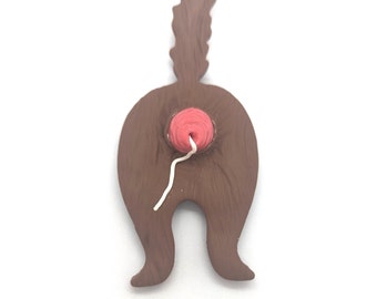 May include: A brown ceramic figurine of a cat's rear end with a pink tail and a white string hanging out.