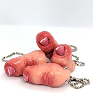 May include: Four fleshy, pink finger-shaped charms with white nail polish on the tips, attached to a silver chain.