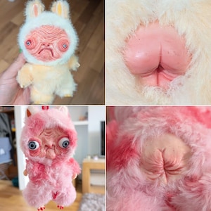 May include: A handmade plush doll with a unique, unsettling design. The doll features a humanoid face with large, expressive eyes and a rabbit-like hood. The body is covered in soft, fluffy fur in shades of yellow and pink.