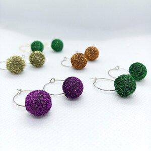 Può includere: Un set di sei orecchini a cerchio con ciondoli a sfera scintillanti in verde, oro, arancio e viola.