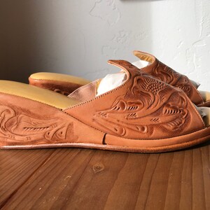 May include: A pair of brown leather wedge sandals with intricate floral carvings. The sandals have a closed toe and an open heel.