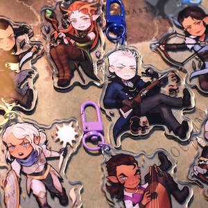 May include: Seven colorful character keychains with clear plastic backgrounds. Each keychain features a different character with unique details and accessories. The characters include a dark-haired elf, a blonde elf, a human with a sword, a human with a lute, a human with a gun, a human with a bow and arrow, and a dwarf with an axe.