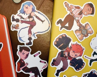 May include: A set of nine colorful cartoon character stickers featuring various characters from the popular video game League of Legends. The stickers are printed on white paper and have a glossy finish.