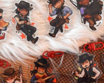 Puede incluir: Una colección de siete llaveros de acrílico transparente con ilustraciones estilo caricatura de personajes con atuendo del oeste. Cada llavero incluye un mosquetón de plástico rojo y muestra figuras con accesorios como sombreros, armas y guitarras.