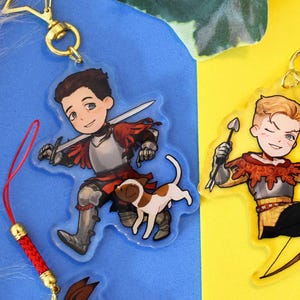 Puede incluir: Dos llaveros de acrílico con personajes de dibujos animados. Uno muestra a un guerrero de pelo oscuro con armadura plateada, una espada y un perro pequeño marrón y blanco. El otro muestra a un arquero rubio con arco y flecha en armadura.