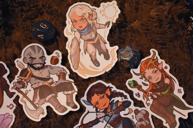 May include: Four illustrated stickers featuring fantasy characters. The stickers are on a brown fuzzy surface. The characters are a woman with blonde hair and a white outfit, a man with brown hair and a brown outfit, a woman with brown hair and a blue outfit, and a woman with brown hair and a green outfit.