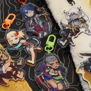 Può includere: Cinque portachiavi con personaggi in stile anime colorati con retro in plastica trasparente. Ogni portachiavi presenta un personaggio diverso con abiti e accessori unici. I portachiavi sono attaccati ad anelli metallici con chiusure in plastica colorate.