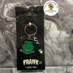 May include: A green and red Frankenstein's monster keyring with the text "FRANK LY I LOVE YOU" on a black backing. The keyring is attached to a silver ring. The packaging includes the text "ENAMEL STYLE KEYRING".