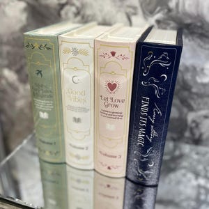 May include: Four hardcover books with decorative spines. The books are in pastel colors: green, cream, pink, and navy blue. The spines feature text and illustrations, including the phrases "Myths, Fairy Tales & Legends", "Good Vibes", "Let Love Grow", and "Finds Its Magic".
