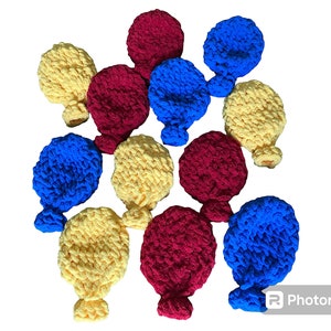 May include: A collection of crocheted balloons in yellow, blue, and red. The balloons are arranged in a circular pattern.