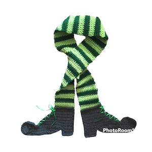 May include: A whimsical, handmade crochet scarf designed to resemble elf legs. The scarf features green and dark green stripes, transitioning into dark gray boots with green laces. A fun and festive accessory.